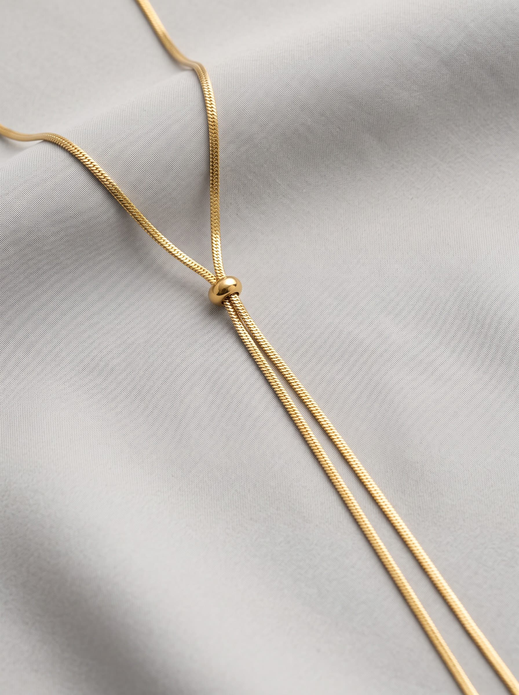 Gold lariat drop chain necklace on grey fabric