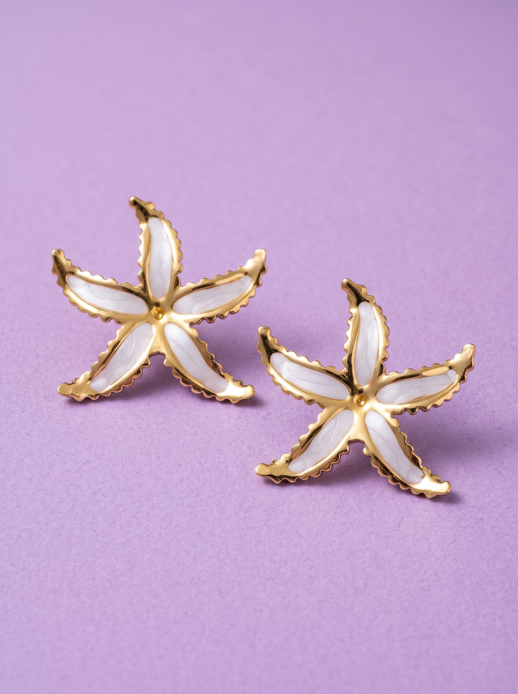 Gold and white enamel starfish earrings on purple fabric